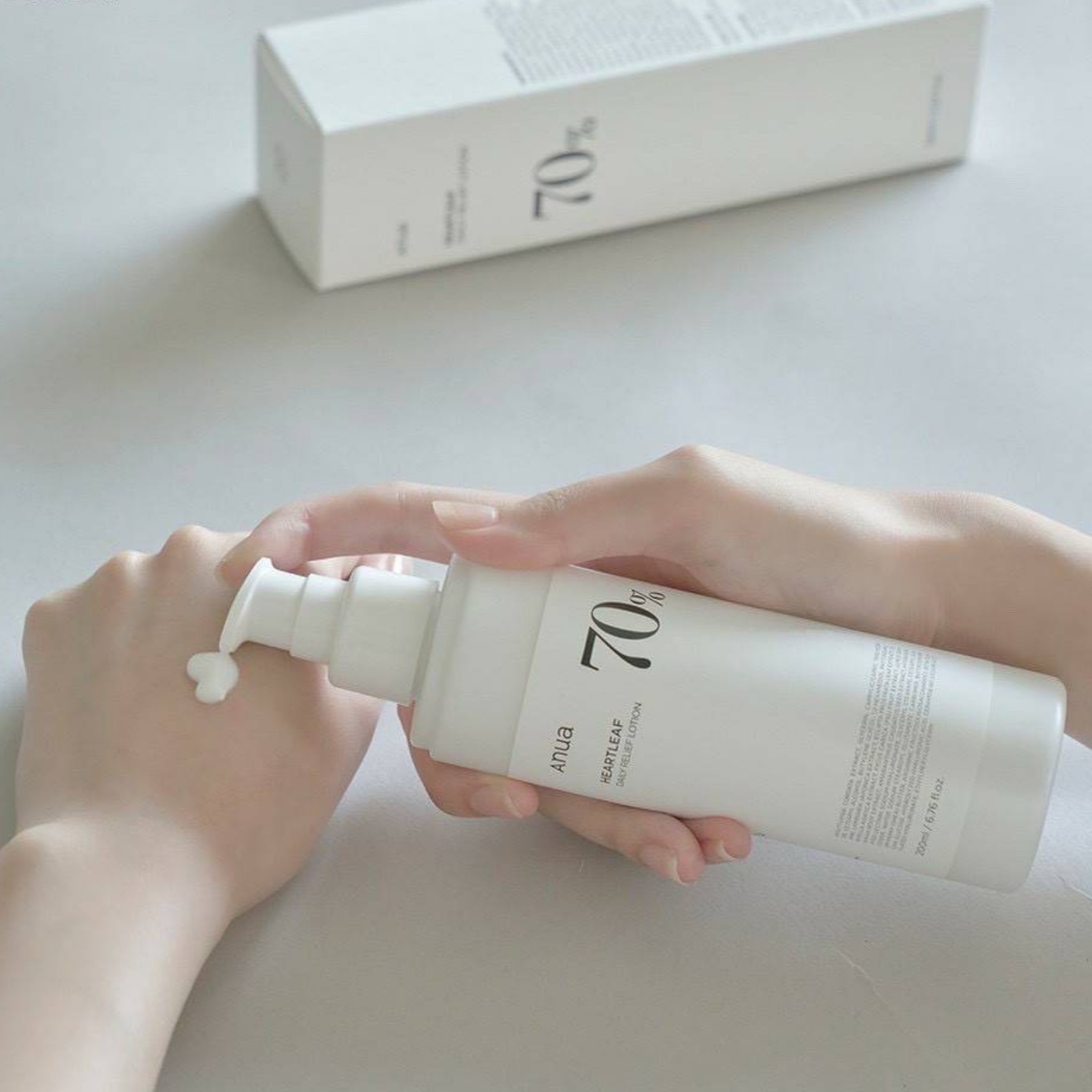 Person holding a white skincare bottle with '70' on it, with a box in the background.