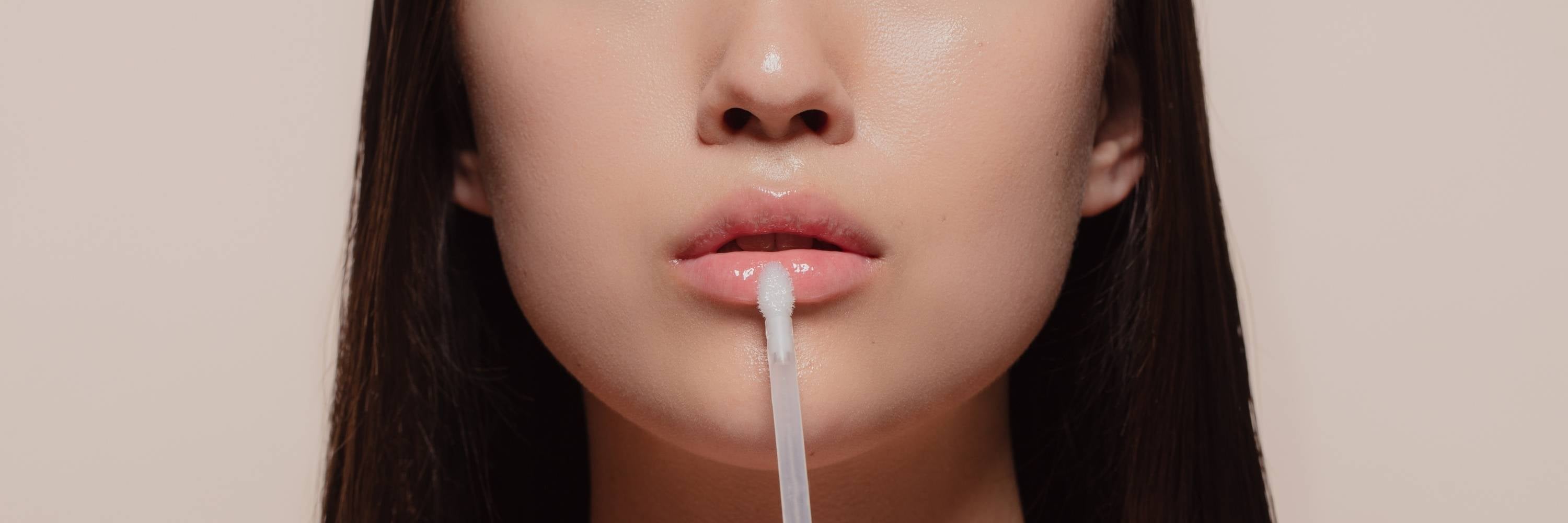 Close-up of a person using a lip balm applicator on their lips against a beige background