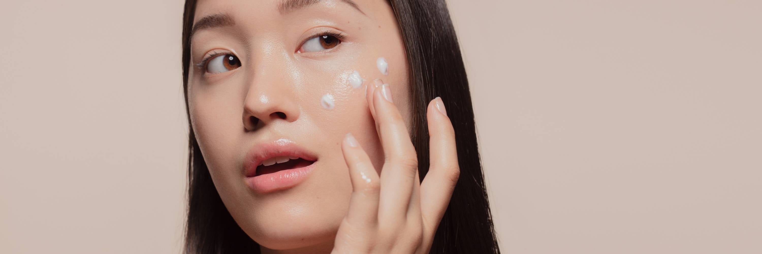 Woman applying moisturizer to her face with a beige background