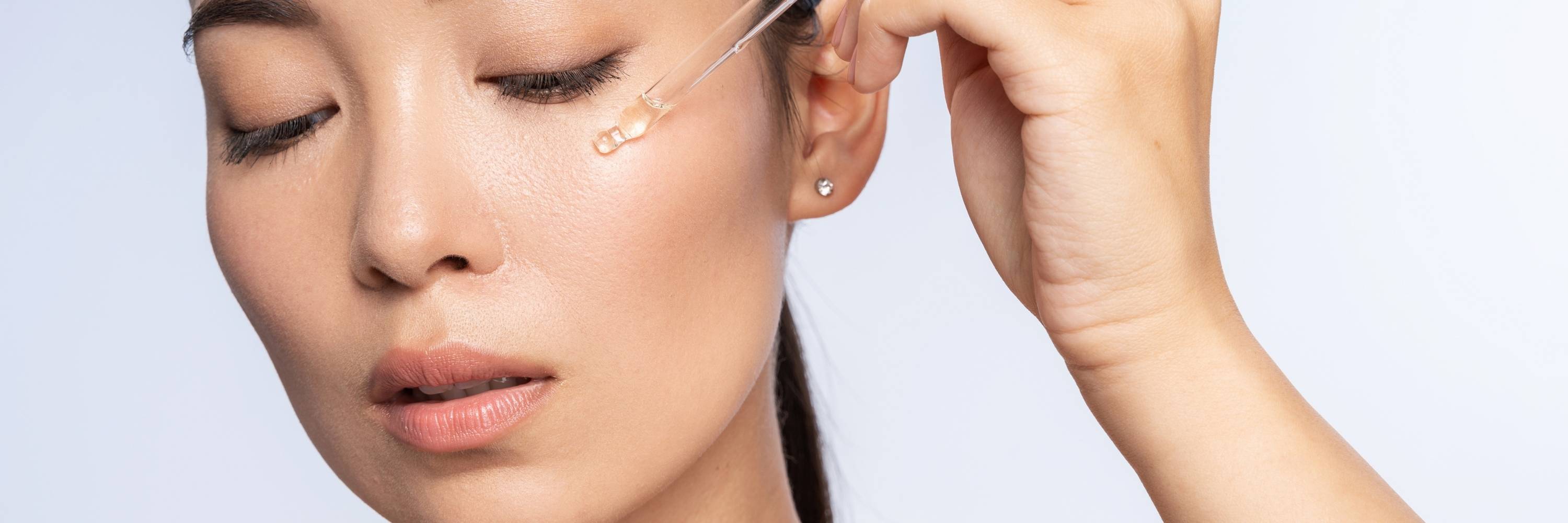 Person applying serum to face with a small applicator on a light gray background