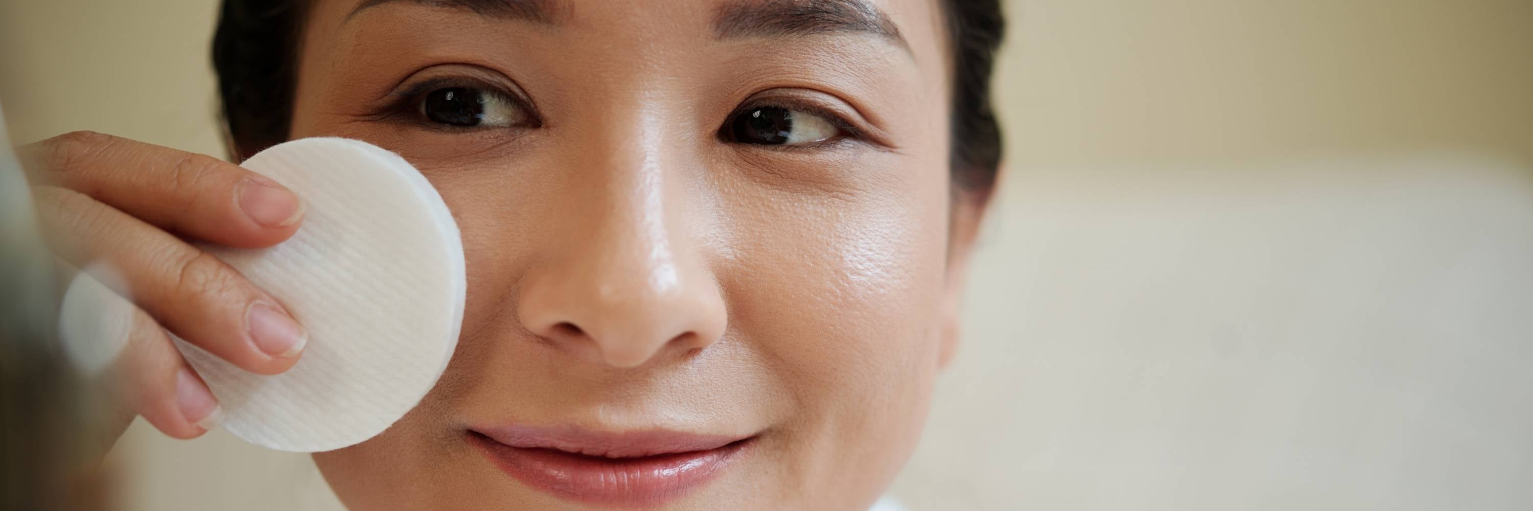 Person applying a toner to their face using a cotton pad.