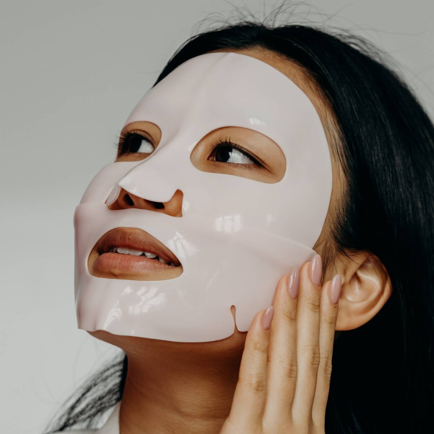 Woman wearing a white face gel mask with a neutral background