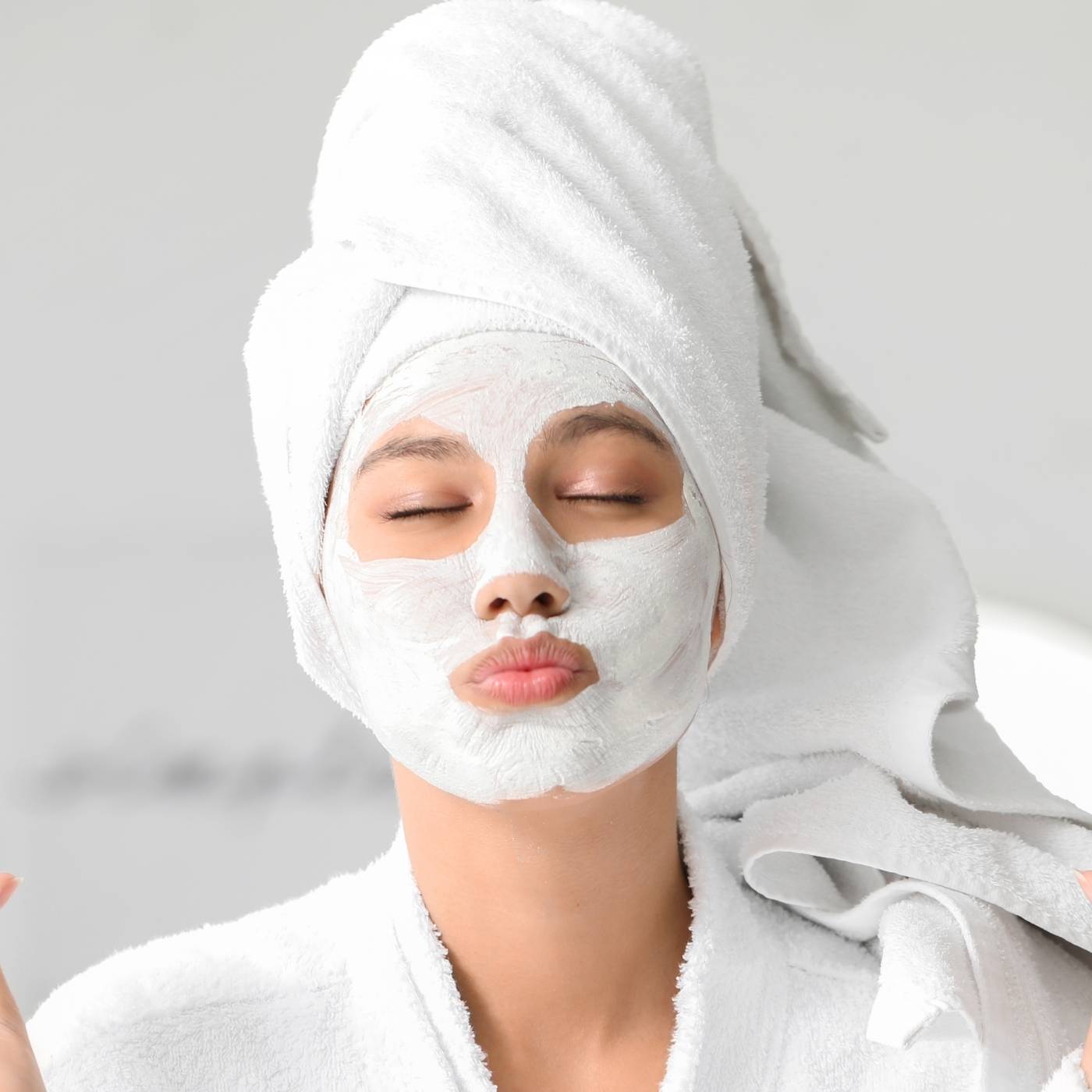 Woman wearing a face mask and white towel on head with gray background