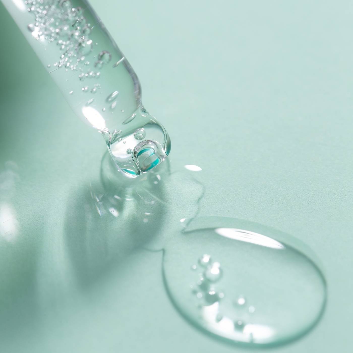 Close-up of a dropper with clear serum on a light green background
