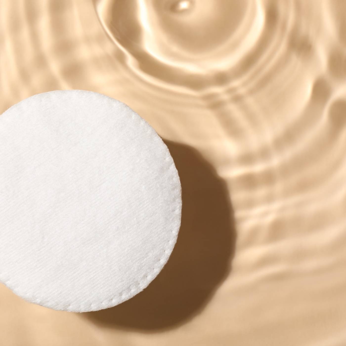 White round cotton pad on a beige textured background