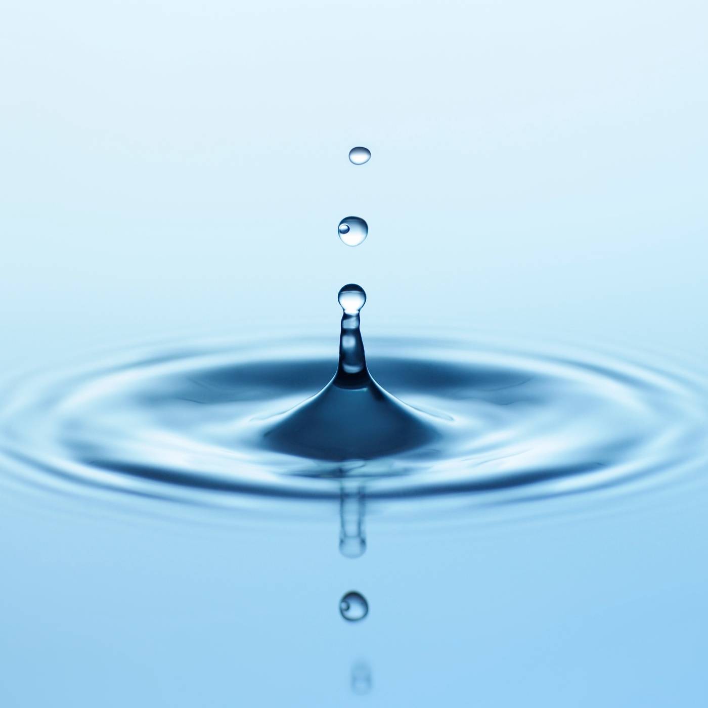 Close-up of a water droplet creating ripples on water with a light blue background