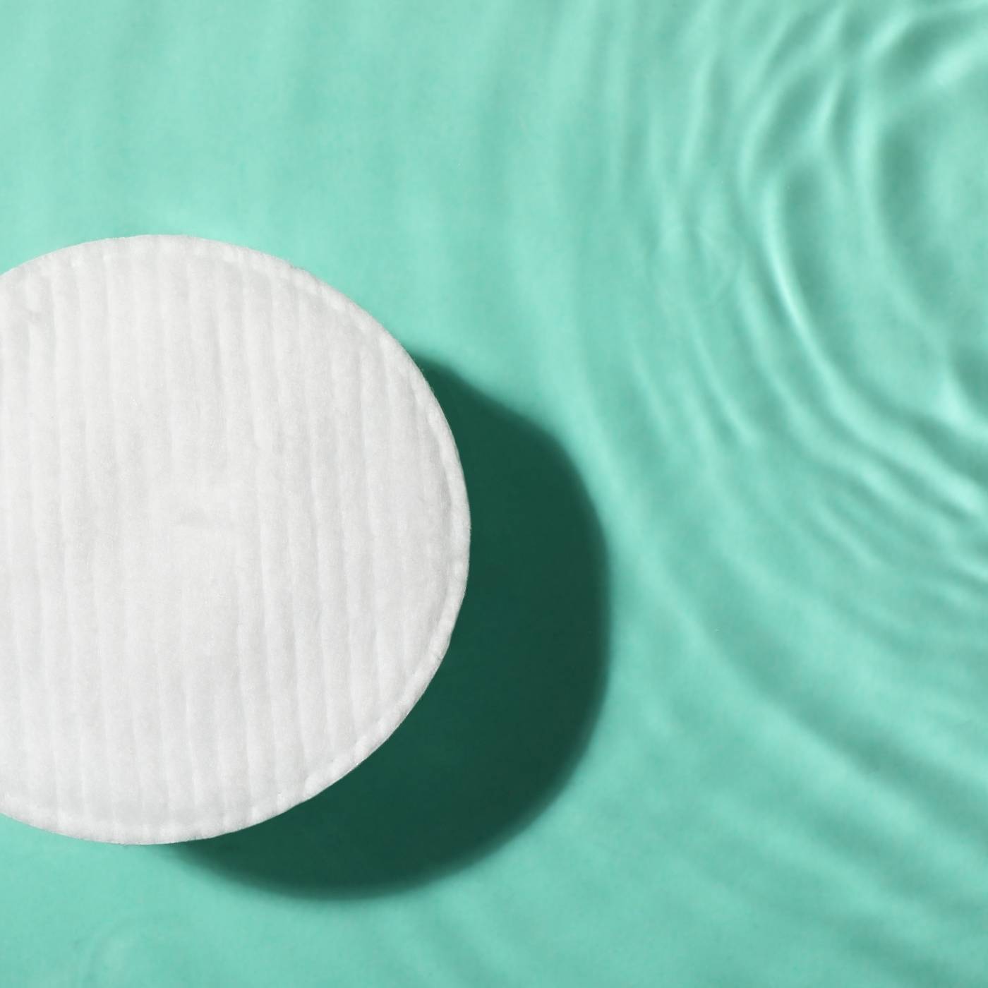 Round white cotton pad on a textured teal surface