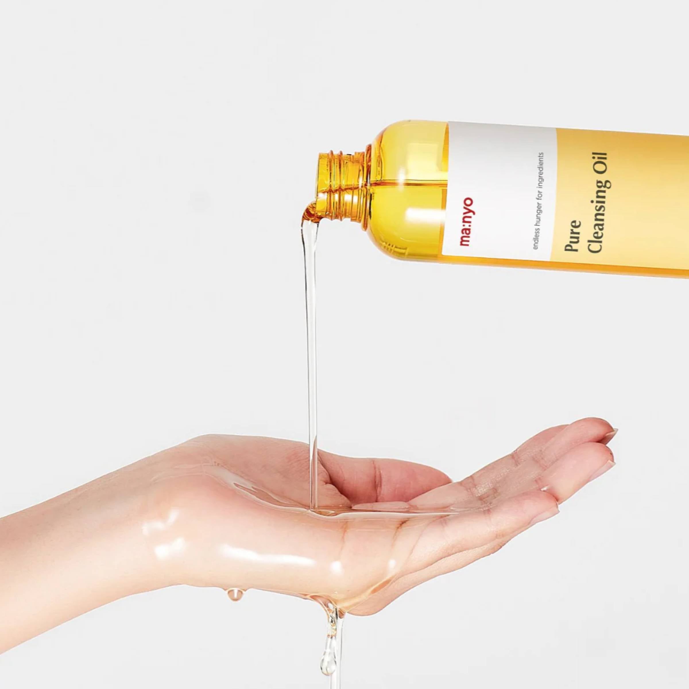 Hand pouring yellow cleansing oil from a bottle labeled 'Pure Cleansing Oil' onto a palm against a light gray background.