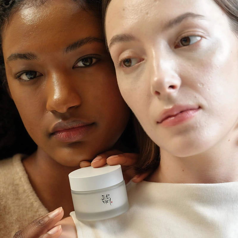 Two women holding a jar of cream against their faces