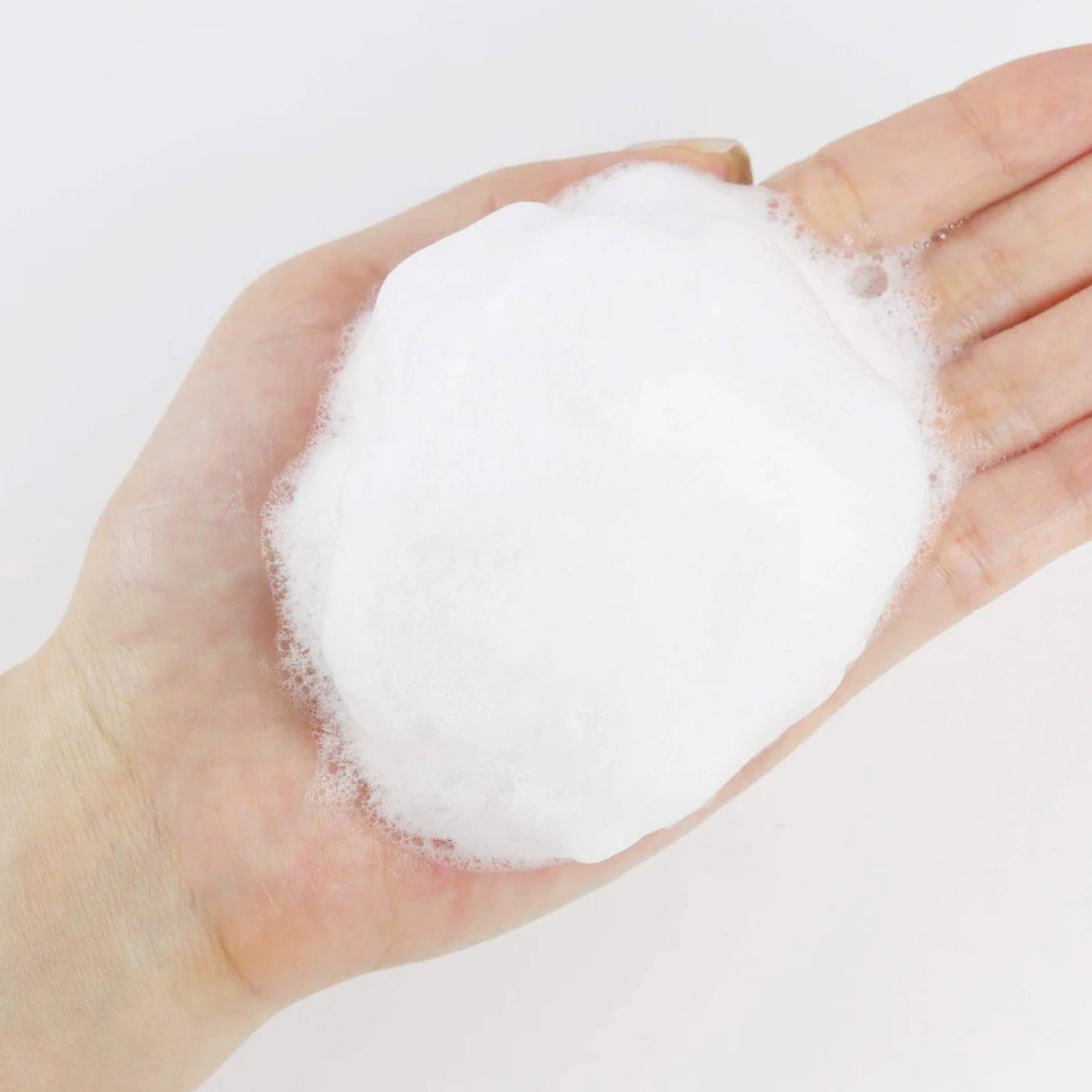 Hand holding cleansing foam against a light background