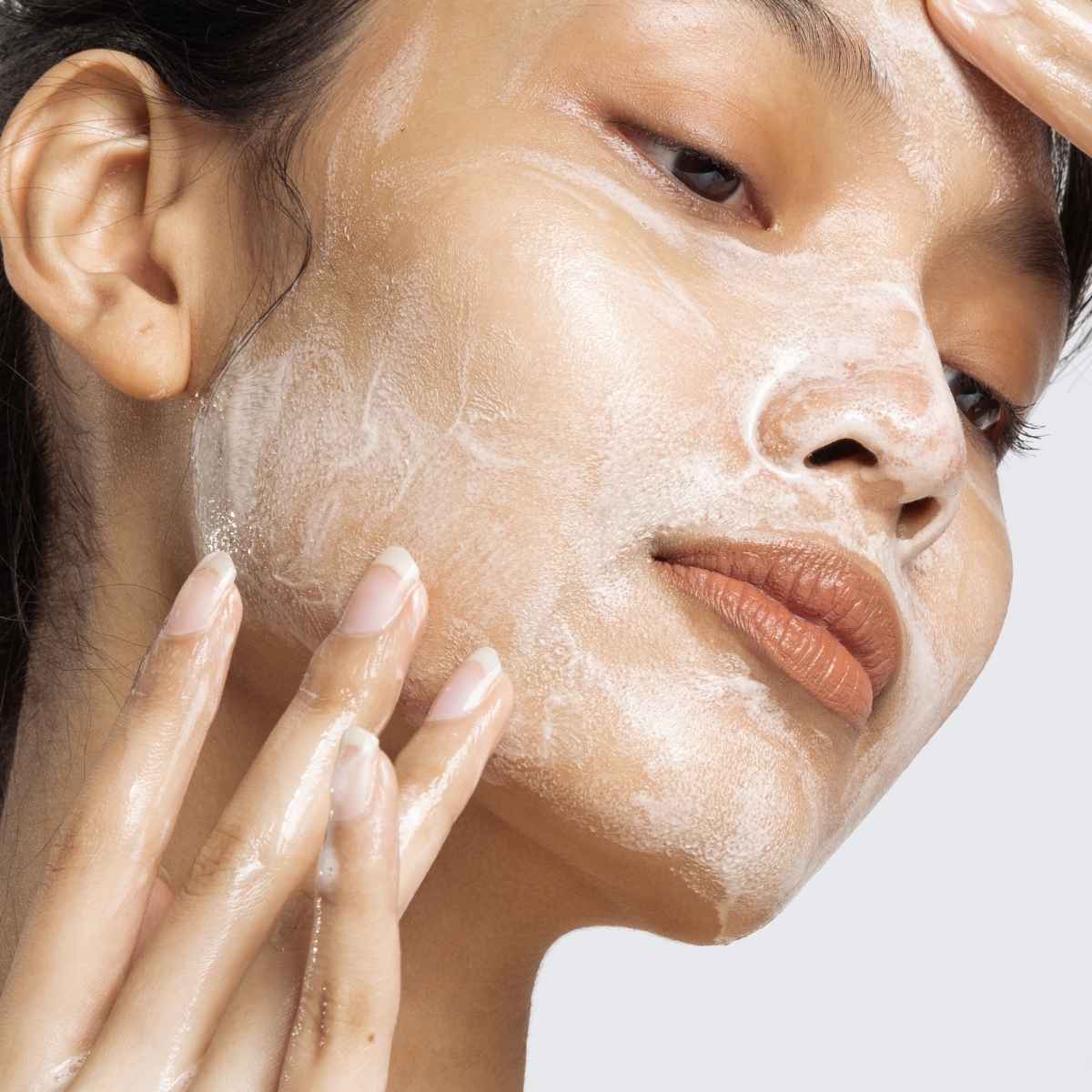 Close-up of a person applying korean skincare cleanser on a neutral background