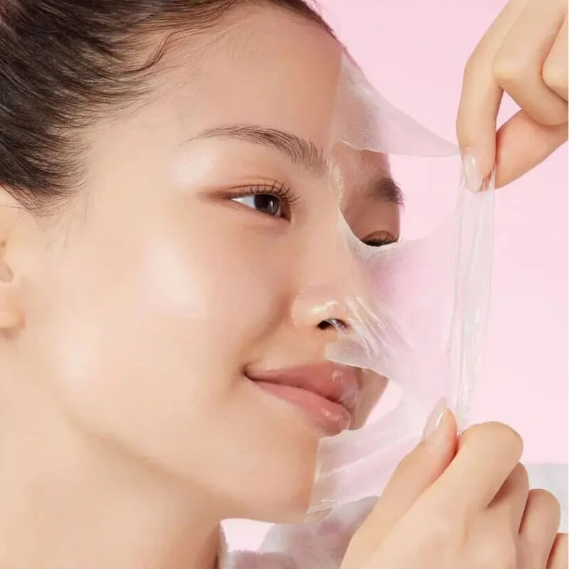 Person applying Medicube Collagen Night Wrapping Mask to their face with a pink background