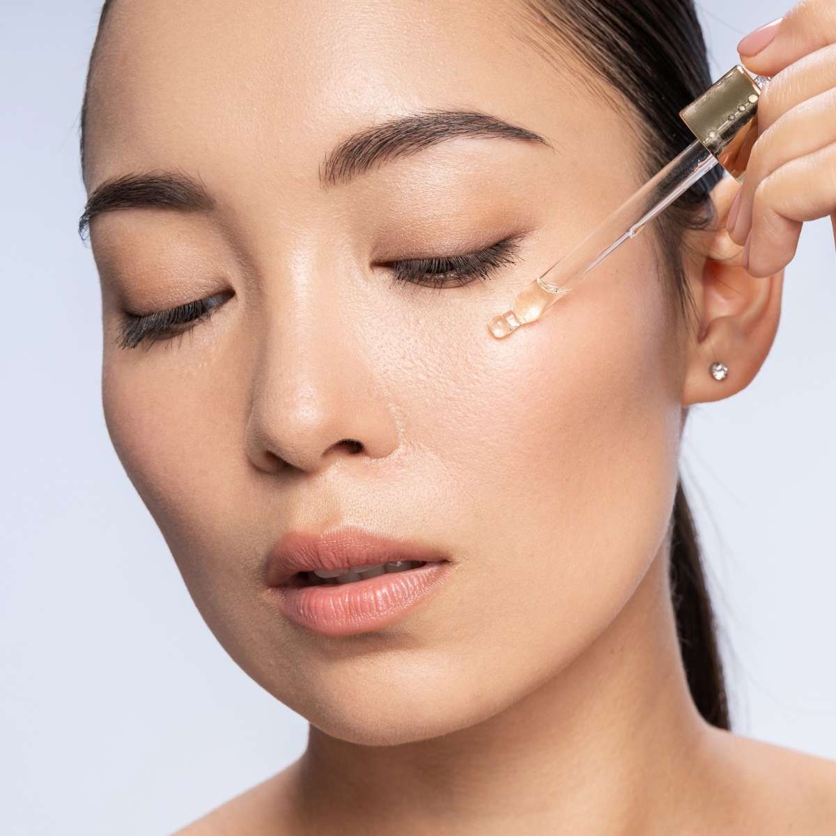 Close-up of a person applying korean skincare serum on a neutral background