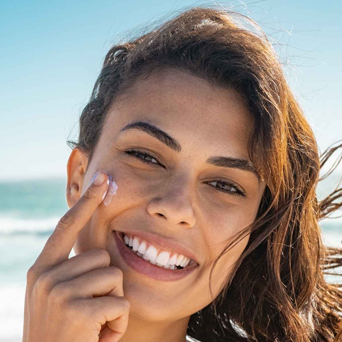 Close-up of a person applying korean skincare sun cream with beach in the background