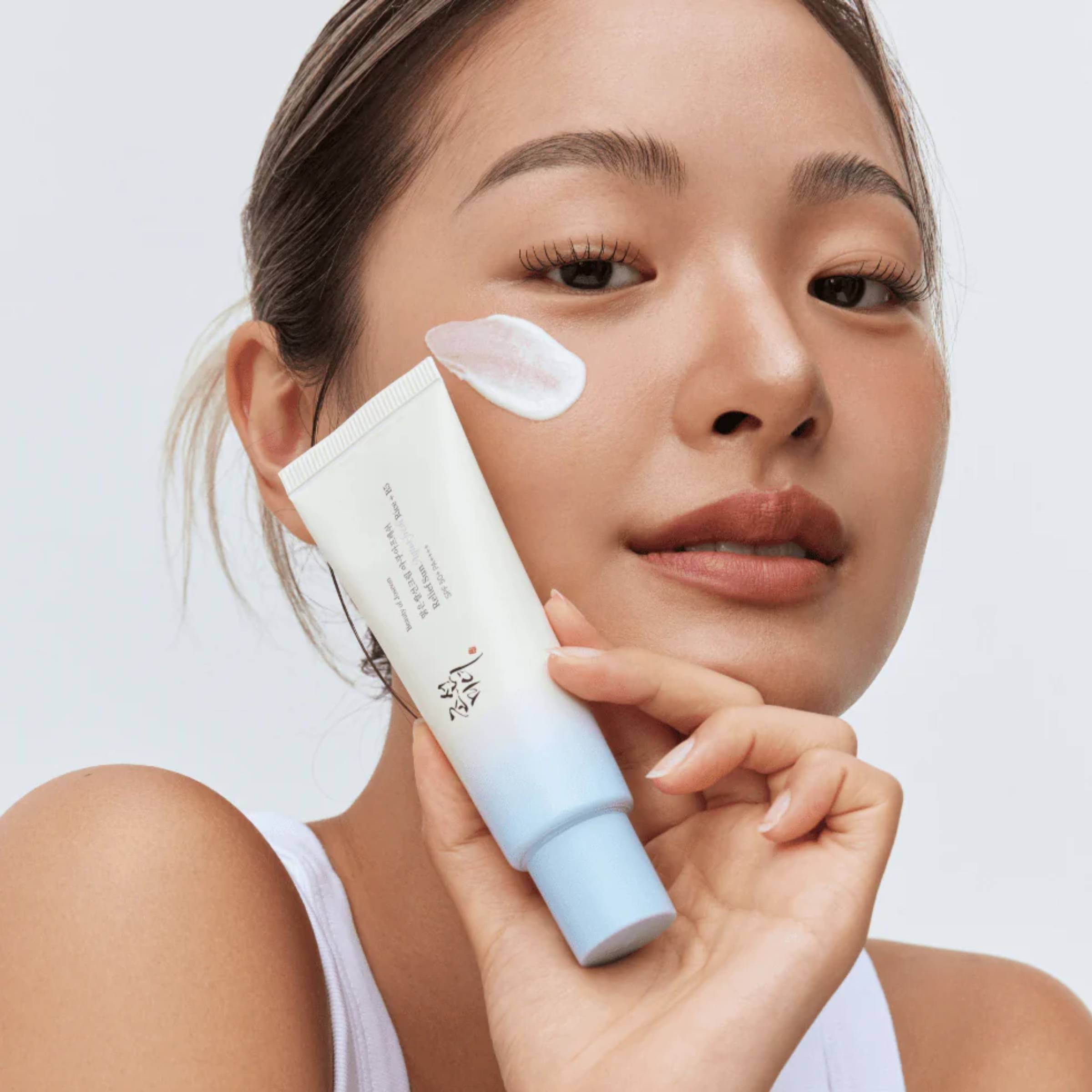 Woman applying sun cream to her face with a white background