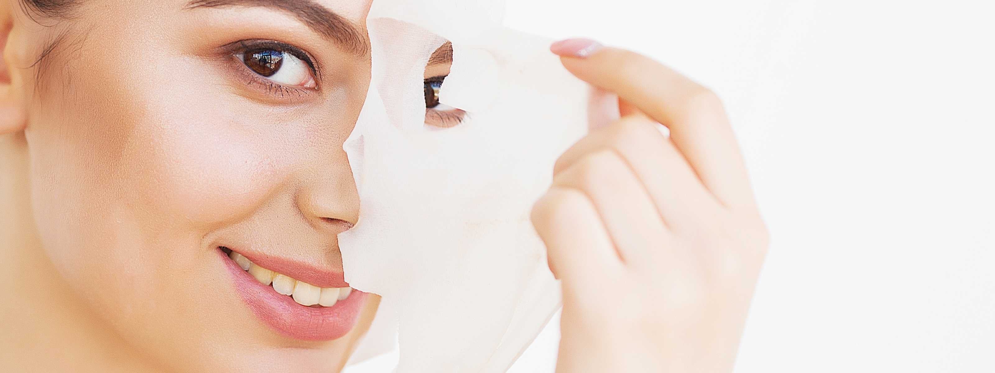 Woman applying a white face mask to her face with a neutral background