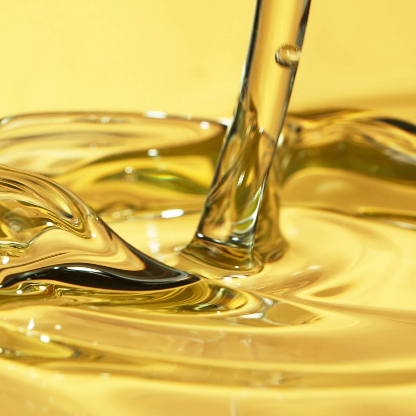 Close-up of golden liquid being poured into a glass container on a yellow background