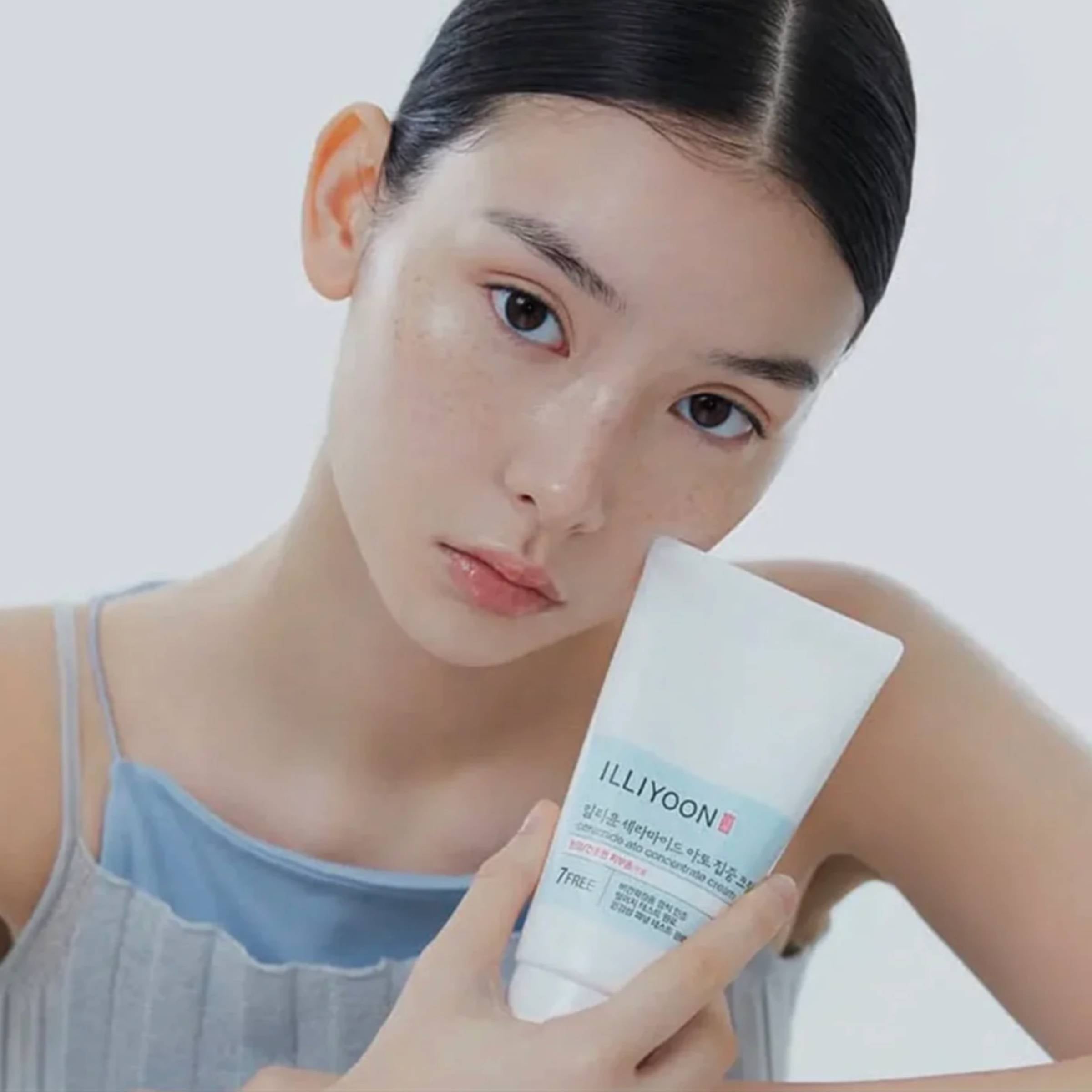 Woman holding ILLIYOON cream tube against a plain background