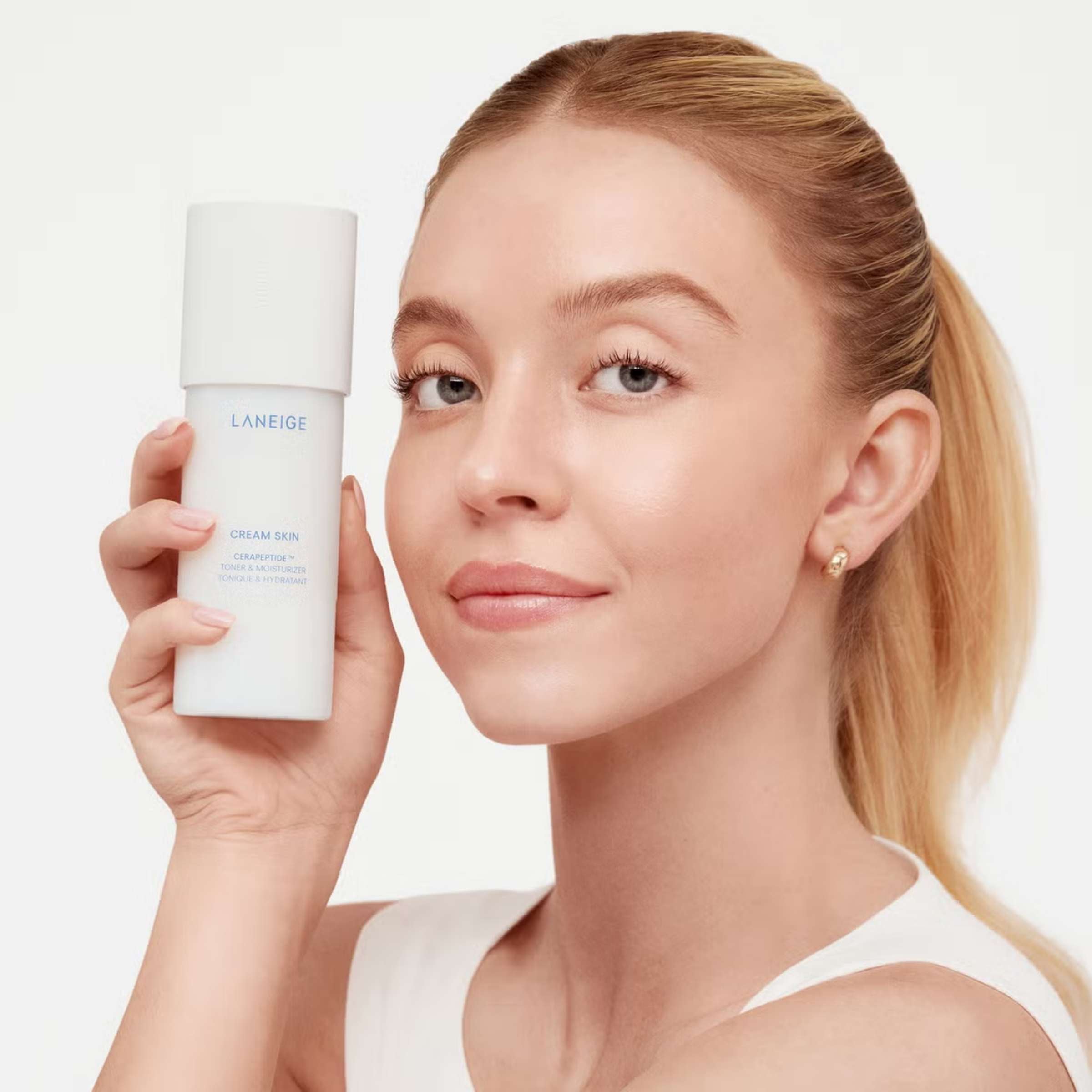 Woman holding a Laneige skincare product against a plain background