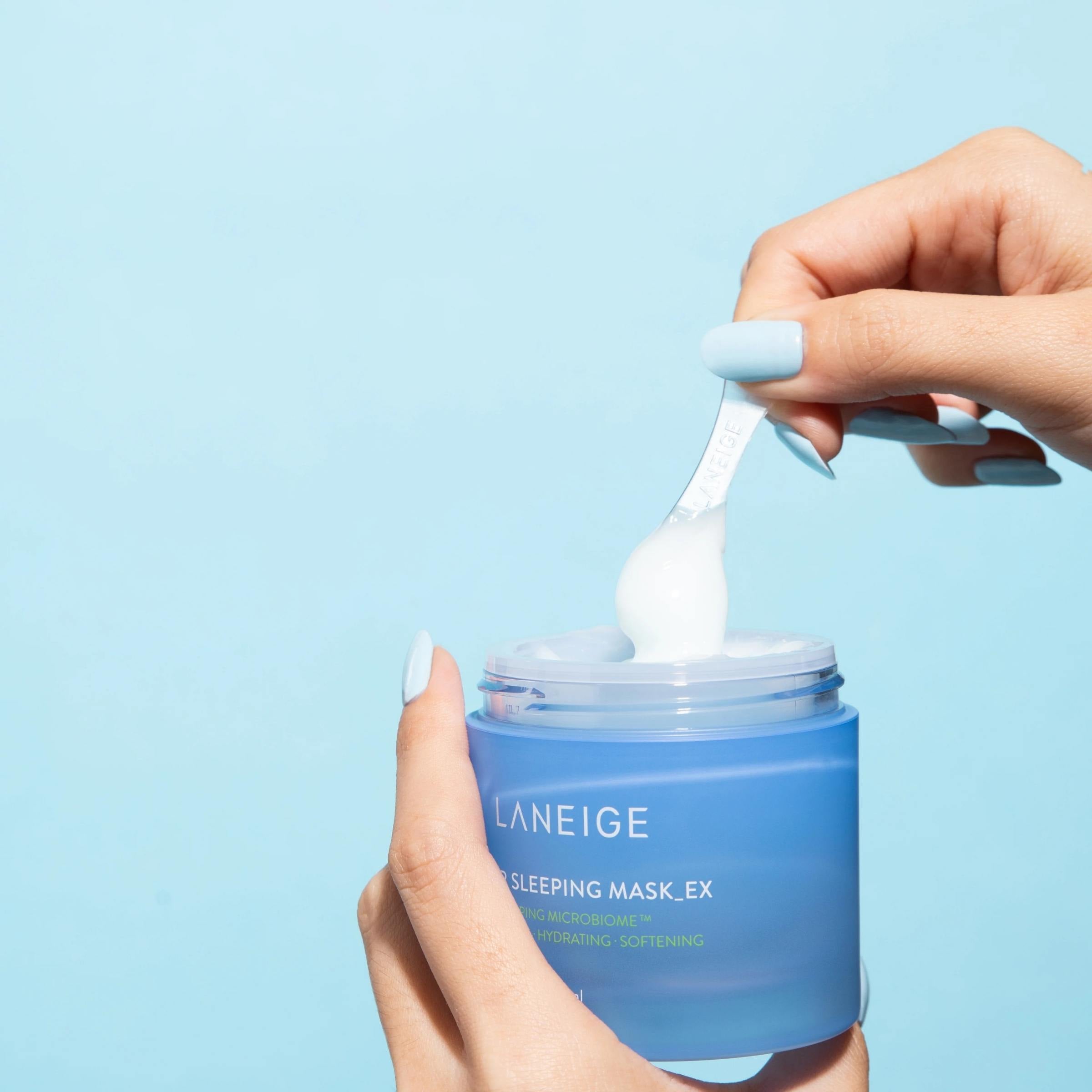 Person using a spoon to take out Laneige sleeping mask from a blue jar against a light blue background