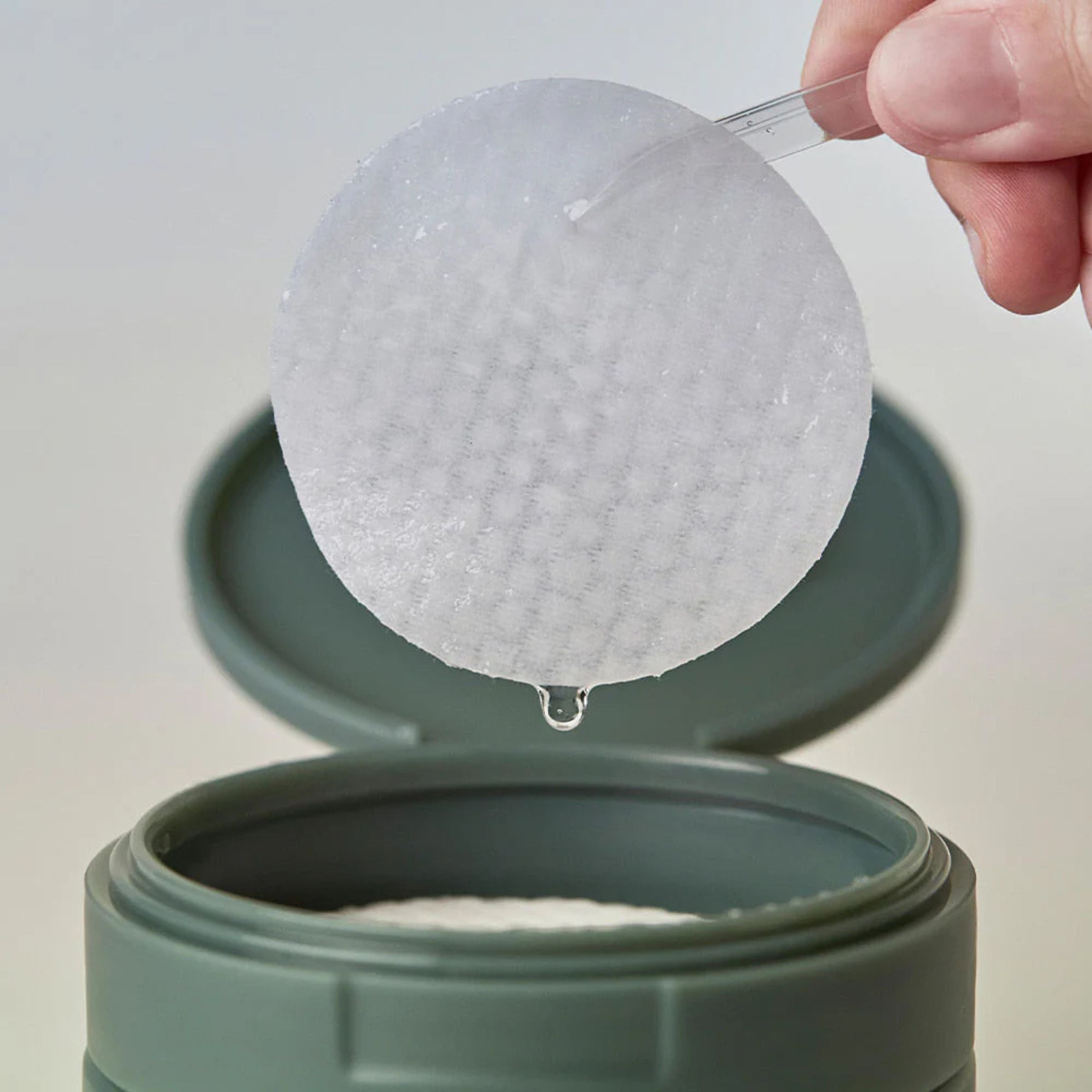 Hand using a spoon to scoop out a white powder from a green container.