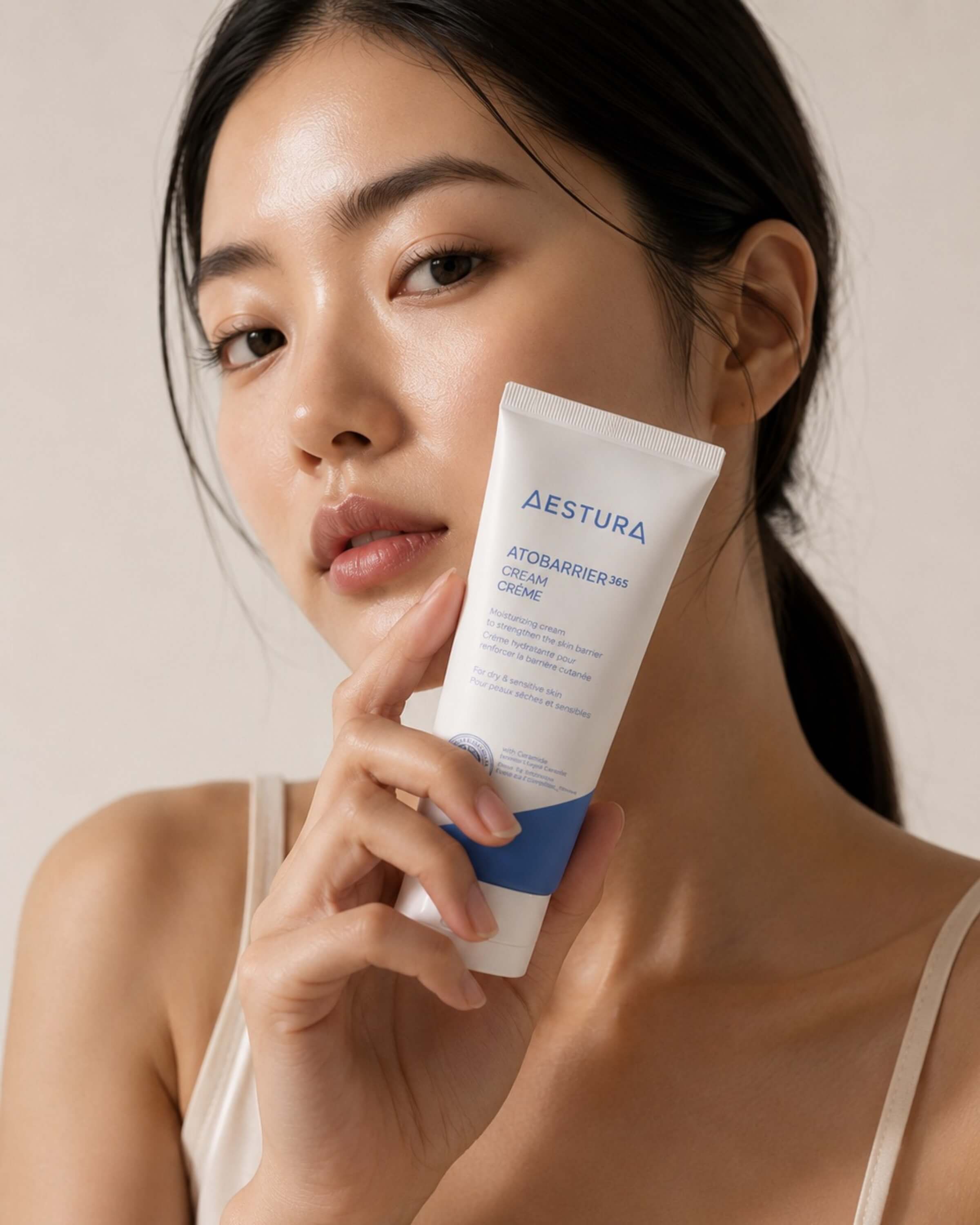 Woman holding a tube of Aestura skincare product against a neutral background
