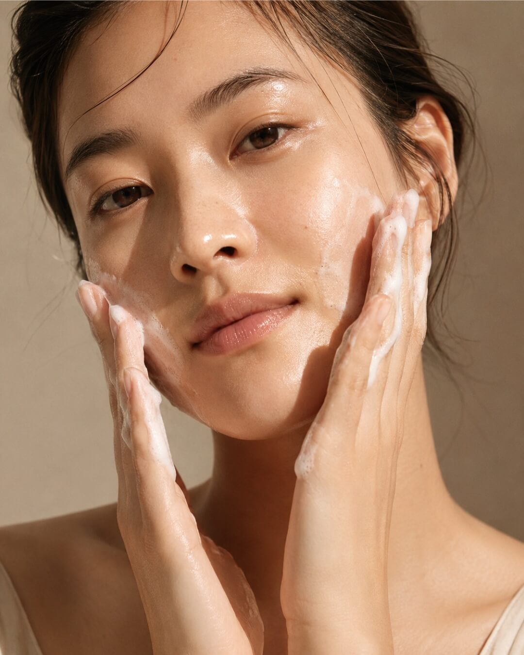 Woman cleansing her face with a neutral background