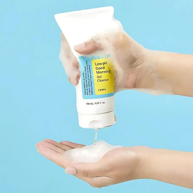 Hand holding COSRX Low pH Good Morning Gel Cleanser with foam being dispensed on a blue background