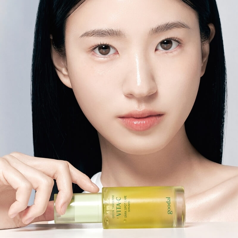 Woman holding a bottle of Goodal Green Tangerine Vita C Dark Spot Care Serum with a neutral background