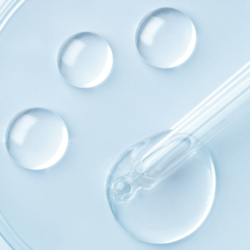 Clear dropper with niacinimide liquid and three droplets on a light blue background