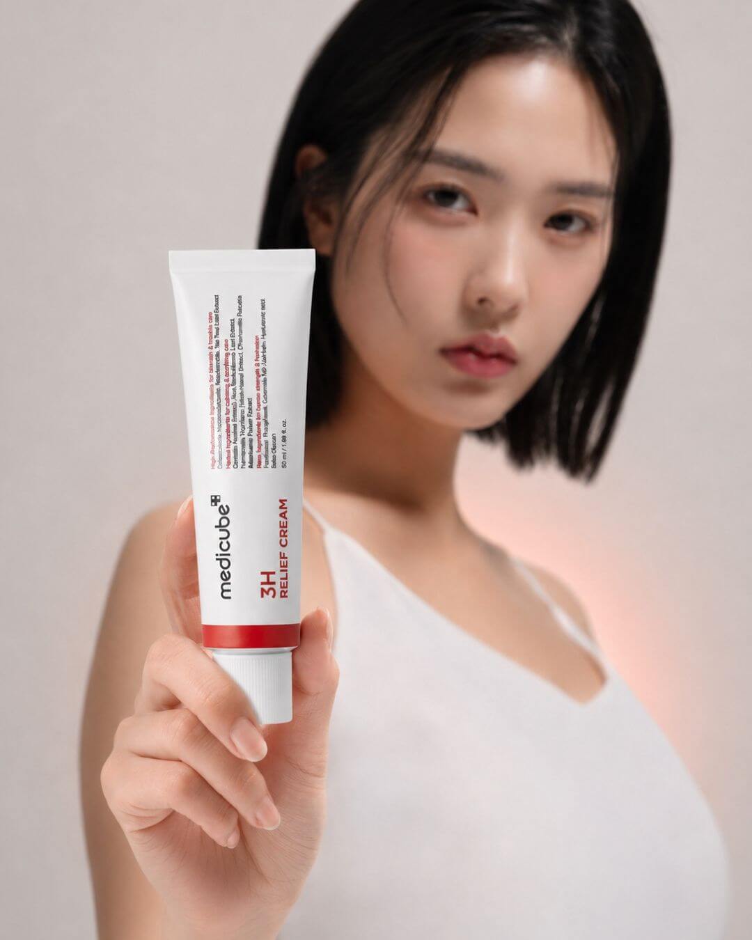 Woman holding a tube of Medicube 3H cream against a plain background
