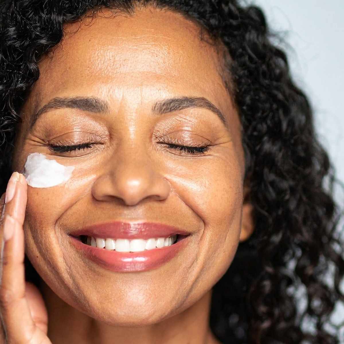 Close-up of a person applying korean moisturizer on a neutral background
