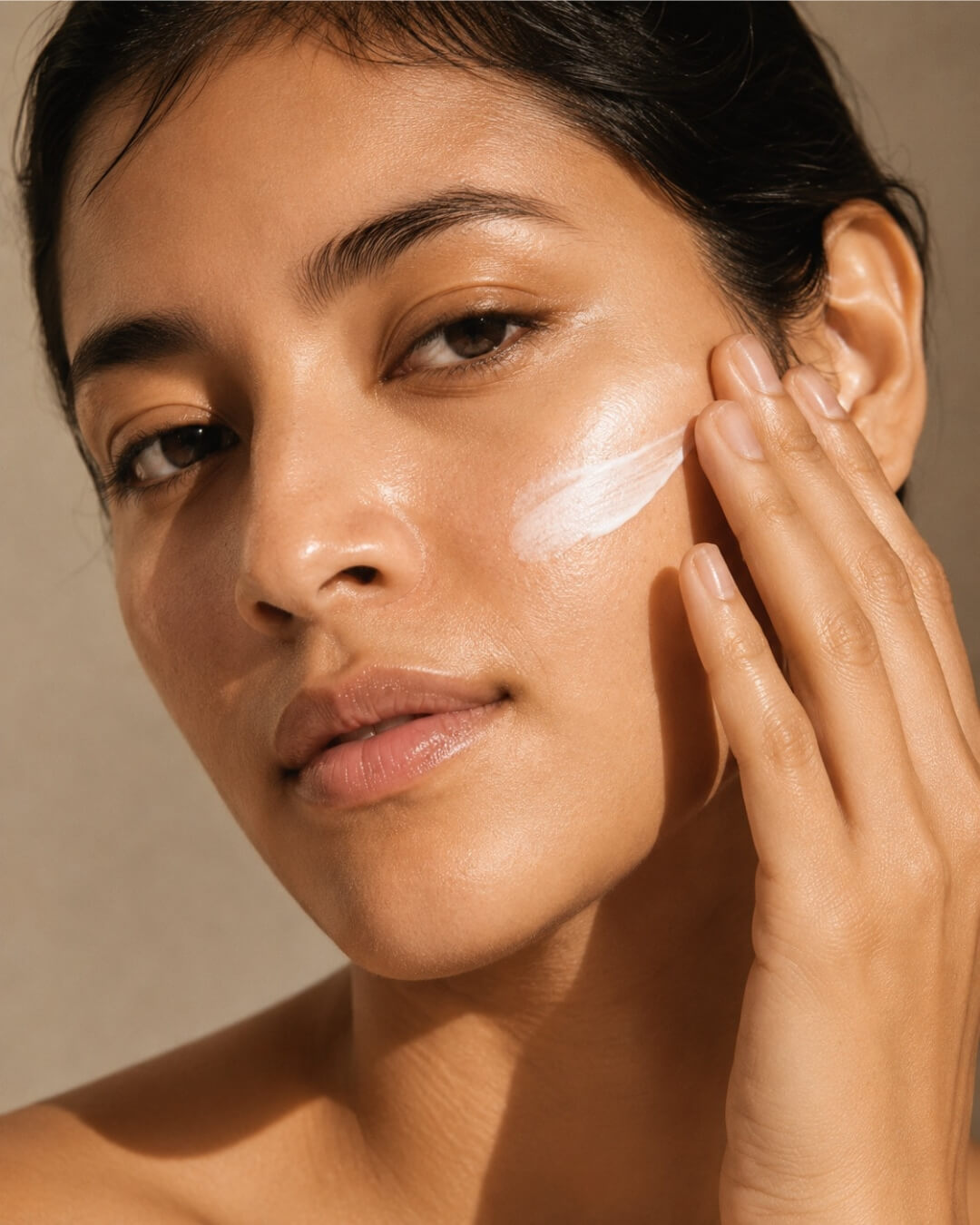 Woman applying sunscreen to her face with a neutral background