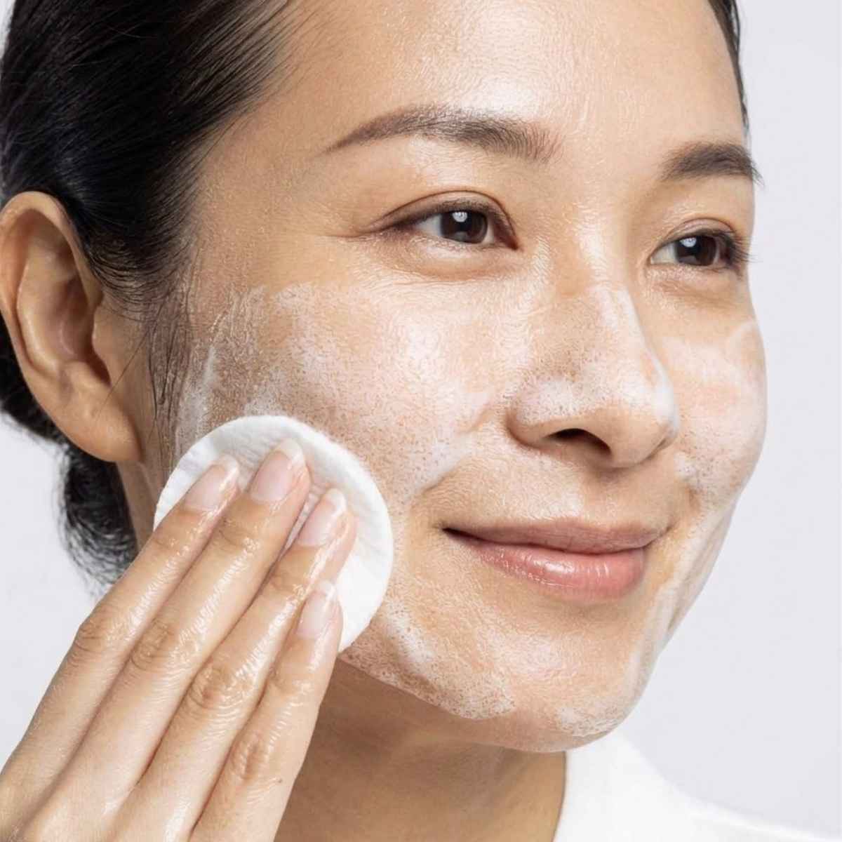 Close-up of a person applying korean skincare toner on a neutral background