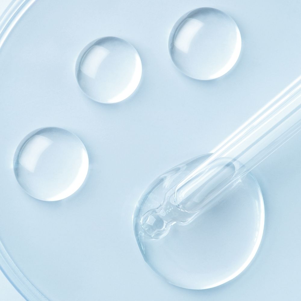 Clear dropper with liquid and three droplets on a light blue background